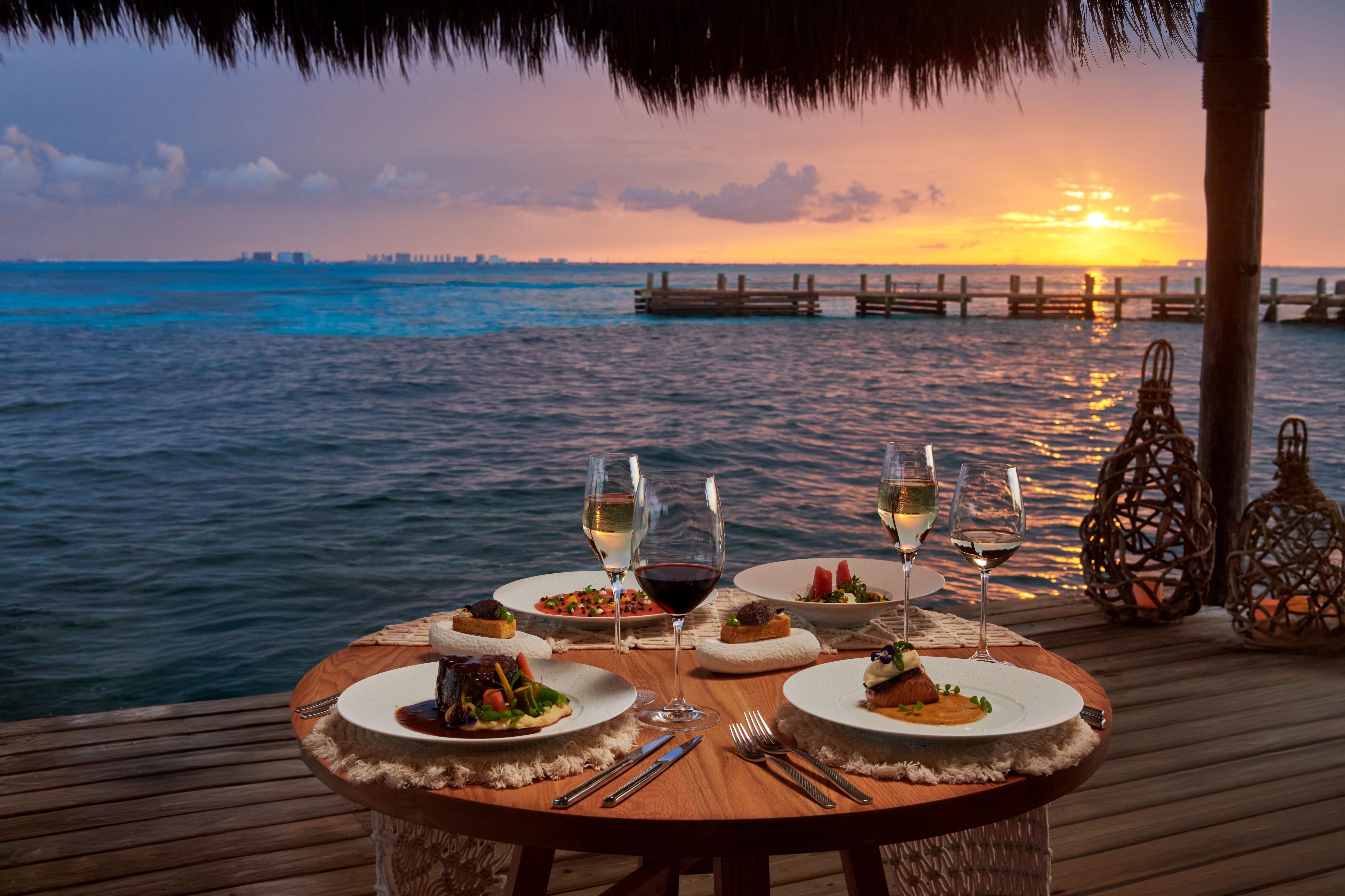 Romantic sunset dining setup at an all-inclusive resort with elegantly set table overlooking the ocean during golden hour